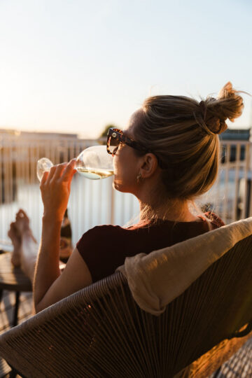 Vrouw drinkt wijn op terras bij zonsondergang